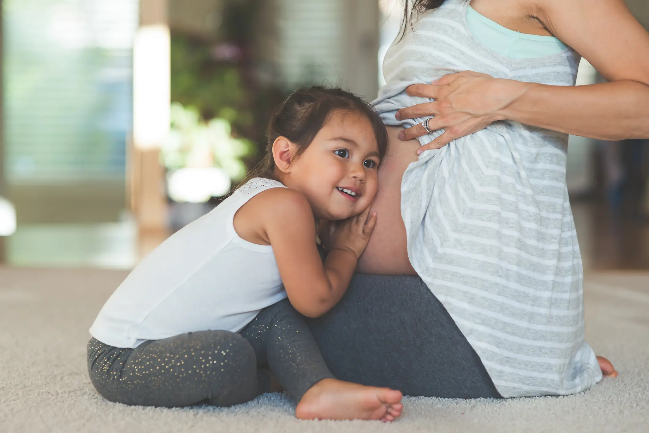 Kind legt Ohr auf Bauch der schwangeren Mutter