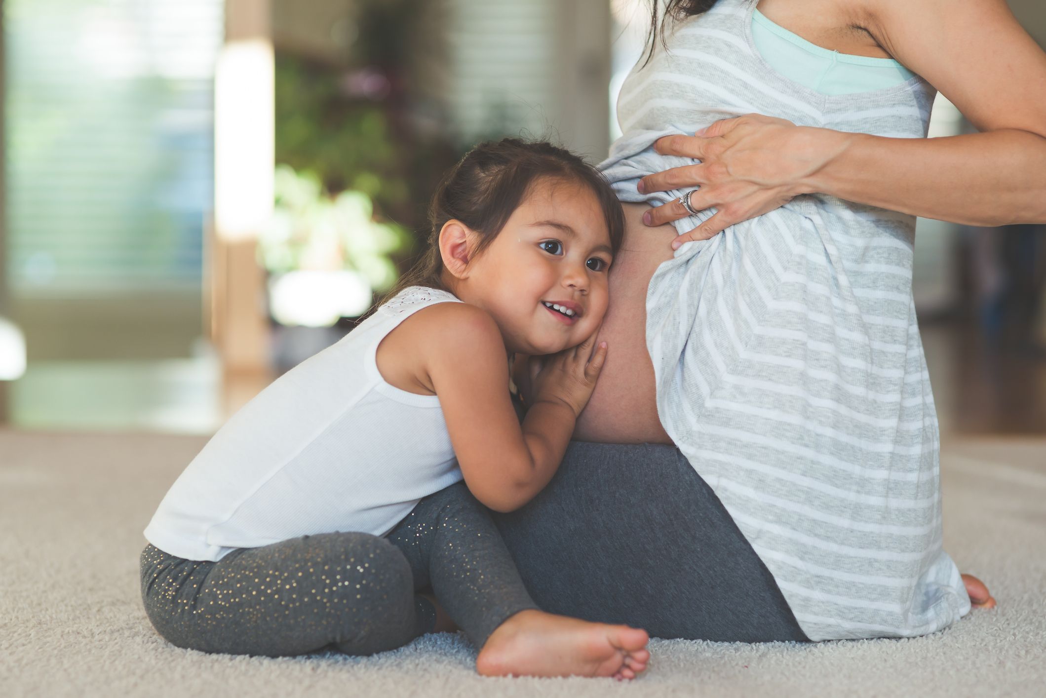 Kind legt Ohr auf Bauch der schwangeren Mutter