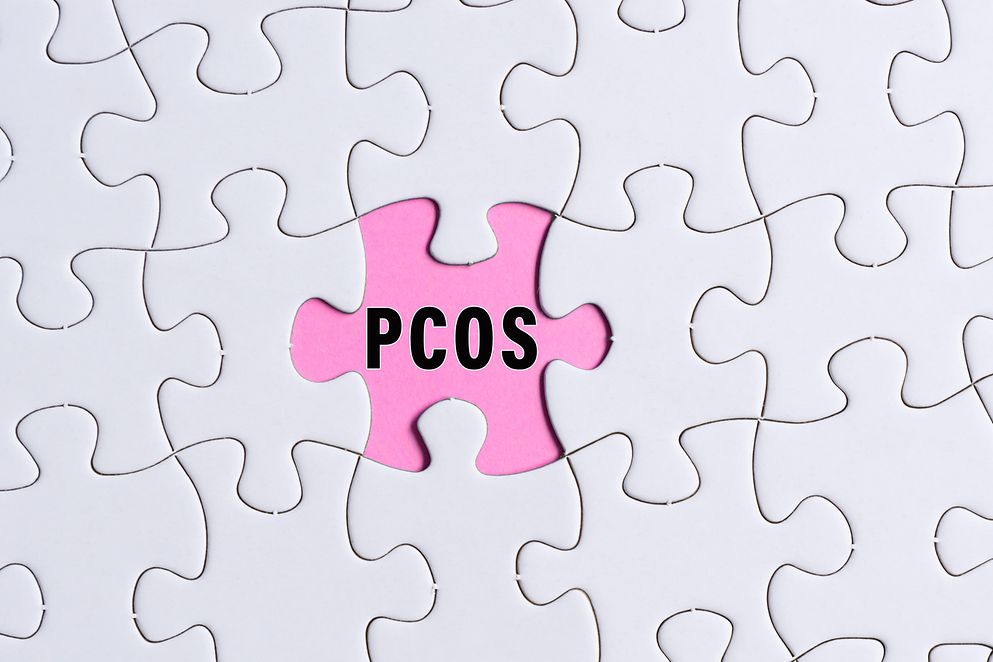 PCOS-Text auf weißem Puzzle über rosa Hintergrund.