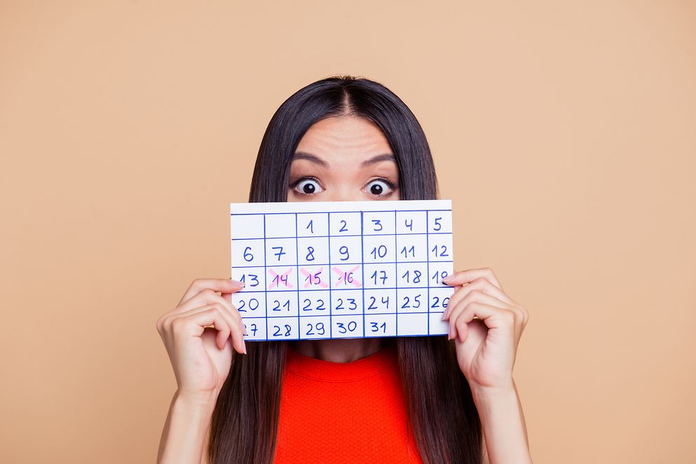 Portrait einer Frau mit erschrockenem Blick, vor ihr Gesicht hält sie einen handgefertigten Kalender aus Papier
