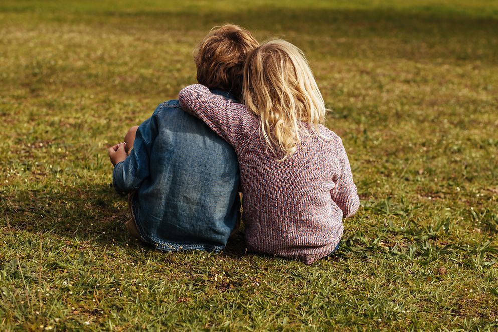 Kleines Mädchen, das neben ihrem Bruder sitzt und ihren Arm auf seine Schulter legt, im Park.